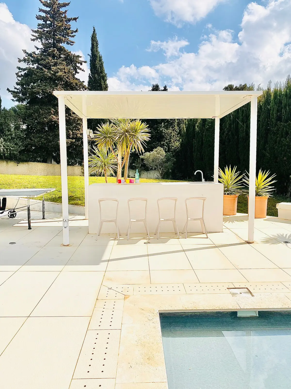 Bar d’extérieur et tabourets sous la pergola blanche